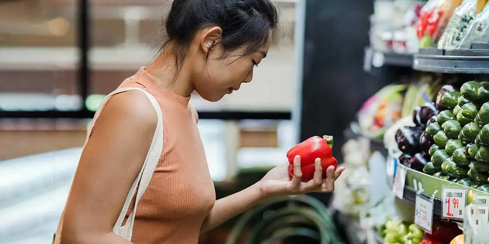 woman grocery shopping holding a red bell pepper